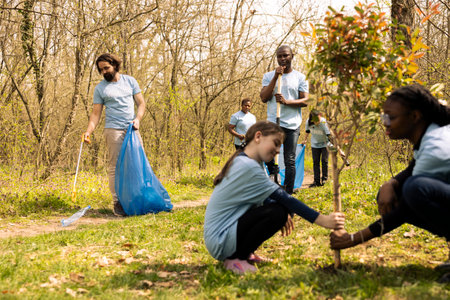 Diverse team of climate activists picking up garbage from the ground, collecting rubbish and recycling plastic in bags. People tidying the forest environment from trash, illegal dumping.の写真素材