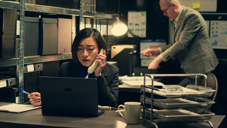 Law officer verifying details for the private investigation, working in archive room. Detective cross checks information on landline phone call, contacting people from records. Camera A.の写真素材