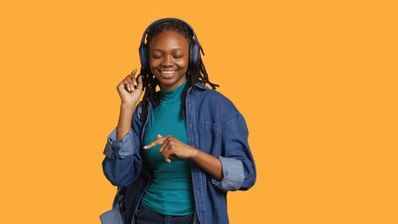 Joyous african american woman doing happy dance, listening music, isolated over studio background. Upbeat person celebrating free time, enjoying music, showing positive demeanor, camera Aの写真素材