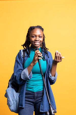 Portrait of happy motivational speaker talking in microphone, addressing audience, using rhetoric to explain, studio background. Cheerful BIPOC teenager using mic, inspiring motivation with speechの写真素材