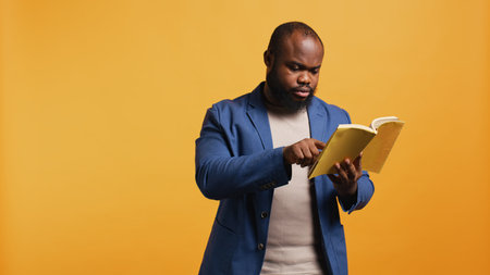 Man struggling to read book with small font, pointing finger to words on page. Person enjoying literature novel, wetting fingers to change page, isolated over studio background, camera Bの写真素材