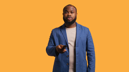 Man zapping through various TV channels, looking for entertaining content to watch, studio background. Person using remote control to select television station, switching between them, camera Bの写真素材