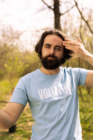 Portrait of sweaty tired male activist taking community service action, digging holes with a shovel to plant trees in the woods. Young volunteers fighting for conservation project.の写真素材