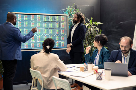 Team of business specialists following stock trade values on interactive board, developing a new financial strategy to increase capital. Forecast affiliates working on organizational success.の写真素材