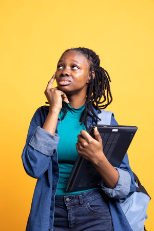 Portrait of woman holding laptop deep in thoughts, pondering during work shift, isolated over studio background. Worker with notebook contemplating how to solve business tasksの写真素材