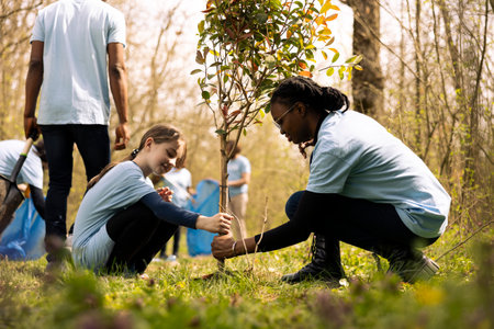 Two diverse activists working together to plant more trees and greenery, filling up ground holes and growing vegetation. Kid and teenager girls collaborating on preserving the environment.の写真素材