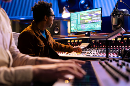 African american audio expert records artist playing piano in studio, using mixing console and...