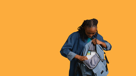 Portrait of upbeat woman searching through backpack, looking for financial graphs papers for school, studio background. Radiant girl taking out business class materials out of rucksack, camera Bの写真素材