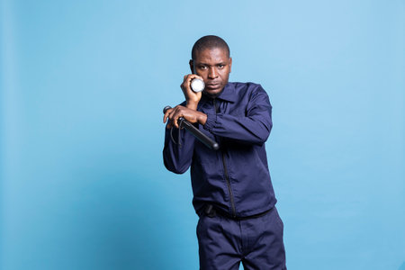 African american security agent on a patrol surveillance in the dark, using a flashlight against blue background. Bodyguard inspecting the perimeter, officer with a lantern for guidance.の写真素材