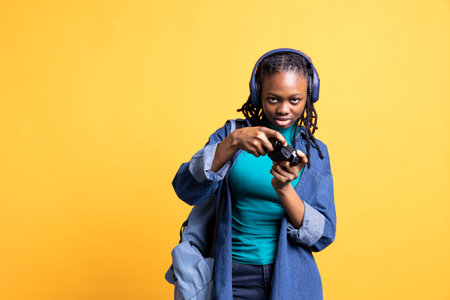 African american gamer holding controller, focused on finishing videogame level, wearing headphones. Woman gaming with gamepad, solving quests, isolated over yellow studio backdropの写真素材