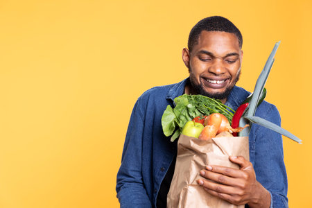 Pleased african american man feels excited about vegan nutrition and bio produce, shopping for natural fresh ethically sourced fruits and veggies. Satisfied smiling guy advertising food.の写真素材