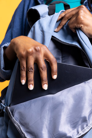 Young girl putting laptop in backpack, preparing to go to school exam, isolated over studio background. Close up shot of pupil packing notebook, preparing for university classesの写真素材