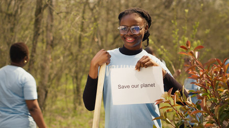 Portrait of african american activist holding poster with save our planet message, spreading environmental care and awareness. Young woman posing with banner to fight ecological justice. Camera A.の写真素材
