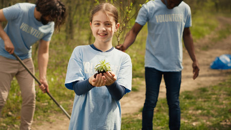 Cute child activist presenting a small seedling tree in her hands, fighting to protect the environment and natural ecosystem. Little girl working to conserve nature and plant trees. Camera A.の写真素材