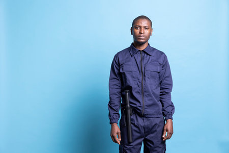 Portrait of african american security officer posing in studio, wearing a patrolling service uniform equipped with a baton for his own protection. Guard on duty shows his authority.の写真素材