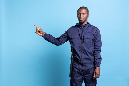 African american serious security agent in uniform pointing to the left side, creates a commercial ad to present something next to him. Guard raising his index finger, indicating a direction.の写真素材