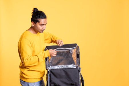 Delivery man arriving to client address, opening zipper to take takeaway order out of thermal backpack. Self employed food courier preparing transportation bag, ready to go to customerの写真素材