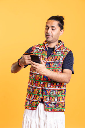 Man looking at credit card to read banking account needed for doing online purchases during sales period. Person wearing traditional indian attire does internet shopping using cellphoneの写真素材