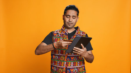 Man adding payment method on shopping website using tablet, taking advantage of promotions, studio background. Indian person buying stuff online using credit card, typing data on device, camera Bの写真素材