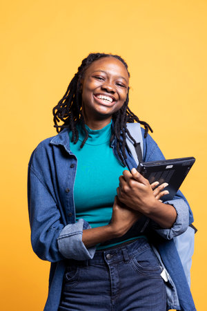 Portrait of smiling BIPOC woman holding laptop, preparing to start work shift, isolated over studio background. Grinning worker with notebook ready to do business related tasks on itの写真素材