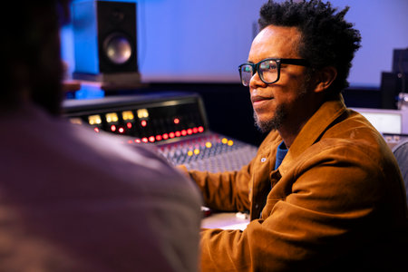 Audio technician and artist collaborating on music for pop rock album, processing and editing sounds...
