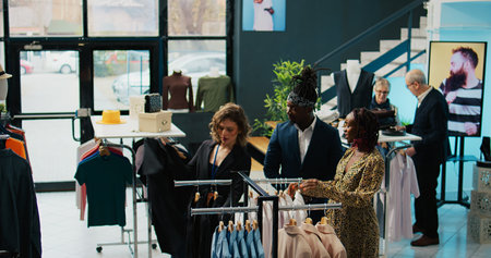 Employees team assisting pregnant woman to find trendy clothes, showing multiple models and colors on hangers. Retail assistants making suggestions for african american customer at store. Camera B.の写真素材