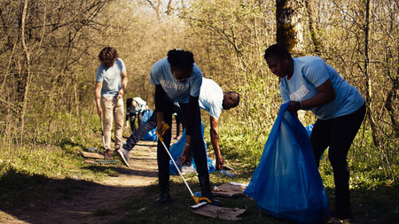 Environmental activists collecting rubbish and plastic waste in garbage bag, using littler cleanup tools to pick up trash from the forest. Women doing voluntary work to protect ecosystem. Camera B.の写真素材