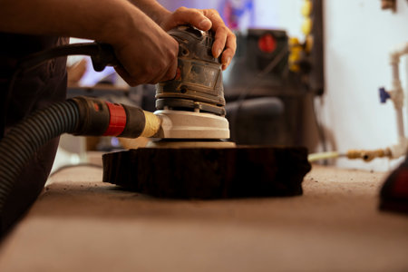Carpenter using orbital sander with fine sandpaper on lumber piece to achieve refined finish. Manufacturer using angle grinder on wood block for professional results, close up shotの写真素材
