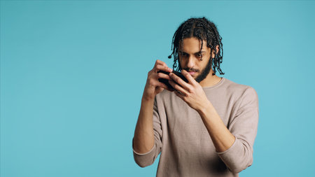 Gamer disappointed after receiving game over screen on cellphone touchscreen display. Middle Eastern man nodding head, upset after losing videogame, playing on phone, studio background, camera Aの写真素材