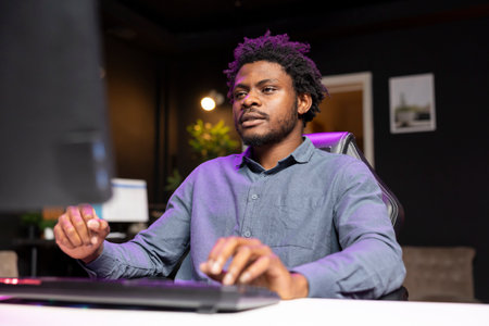 Gamer playing videogames on computer desktop late at night, struggling to stay awake. Man using PC...