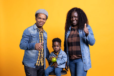 African american mom and dad giving like symbol in front of camera, posing with their adorable son...