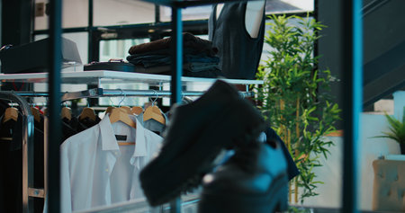 Empty fashion boutique selling new designer collection at shopping mall, having shoes and bags among clothes on stands. Interior of clothing store decorated with trendy tailoring items. Camera B.の写真素材