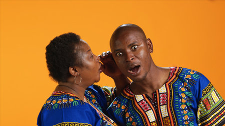 Smiling woman sharing important secret with her husband, whispering in his ear and telling. Shocked man leaning in and listening to confidential information, secrecy concept.の写真素材