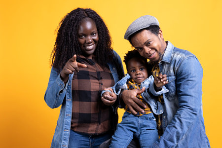 Smiling loving young family with a small cute toddler posing on camera, mom and dad hugging their child against yellow background. Happy peaceful couple with a little baby boy.の写真素材
