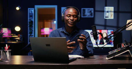 Portrait of BIPOC tech vlogger reviewing newly released smartphone in rgb lights living room studio. Entertaining influencer filming technology channel episode using professional video toolsの写真素材