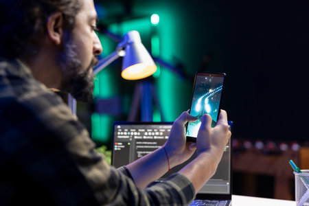 Male programmer taking a break from work, using his mobile device for gaming entertainment. Bearded...