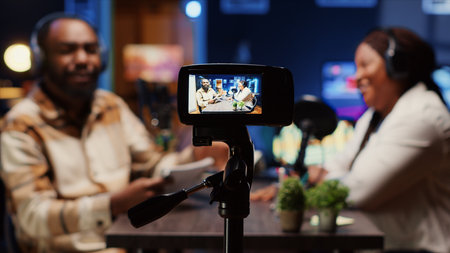 Focus on professional camera used to record radio show presenter live conversation with man in personal studio. Close up on production gear with host and guest talking in blurry backgroundの写真素材