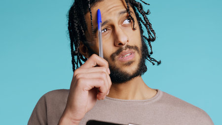 Portrait of man deliberating, putting pen on lips, coming up with idea concept. Thoughtful person reflecting, doing brainstorming, having eureka moment, studio background, camera B close upの写真素材
