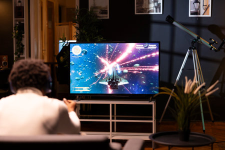 African american man in home theatre using cloud gaming service to play demanding science fiction...