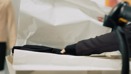 Store assistants receiving new fashion collection to put on display in showroom, looking at clothes from the delivery box at cash register. Employees tea preparing to store new clothing. Camera A.の写真素材
