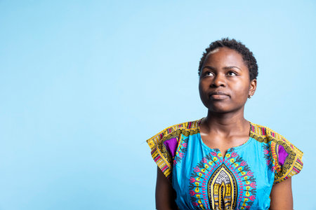 Portrait of serious confident young woman posing in studio, feeling confident in authentic traditional costume. Charming person looking stylish over blue background, natural beauty concept.の写真素材