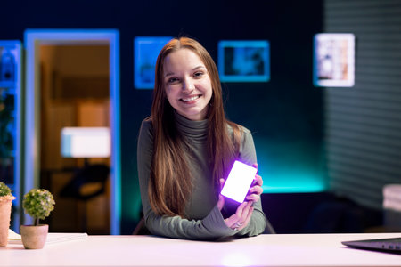 Portrait of smiling influencer in studio using camera to capture live broadcast, reviewing mini RGB lights. Cheerful internet show host films electronics haul, presenting wireless LED lighting deviceの写真素材