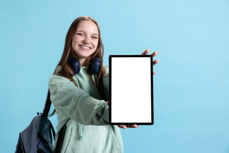 Jolly young girl presenting tablet with isolated screen display, smiling, studio background. Teenager creating ad promotion, showcasing mockup deviceの写真素材