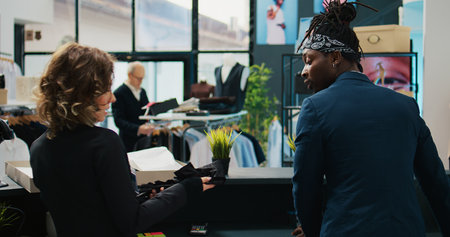 Store assistants receiving new fashion collection to put on display in showroom, looking at clothes from the delivery box at cash register. Employees preparing to store new clothing.の写真素材
