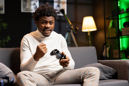 Merry man feeling happy while playing videogames on gaming console with controller, celebrating...