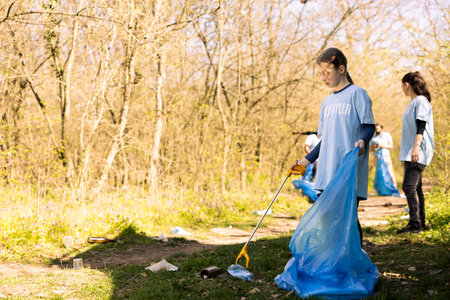 Sweet child volunteer picking up trash and plastic to recycle, working with adults to conserve and restore nature. Little activist combating illegal dumping, collecting rubbish in bags.の写真素材