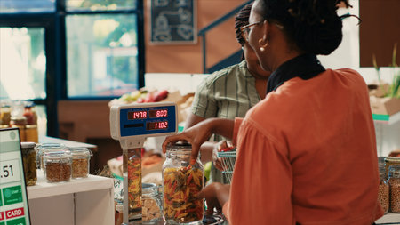 Local merchant weighting and scanning produce for customer at organic farmers market, african american women supporting healthy eating. Buyer shopping for chemicals free vegetables. Tripod shot.の写真素材