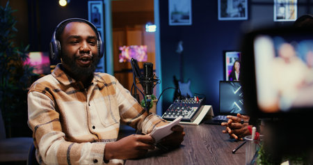 BIPOC man on podcast conversating with guest during marathon stream for charitable cause. Host in apartment studio chatting with celebrity, gathering donations from fans during online showの写真素材