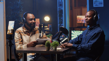 Man recording podcast using smartphone attached to tripod and high tech microphones to interview guest, ensuring flawless video and sound quality for audience watching at homeの写真素材