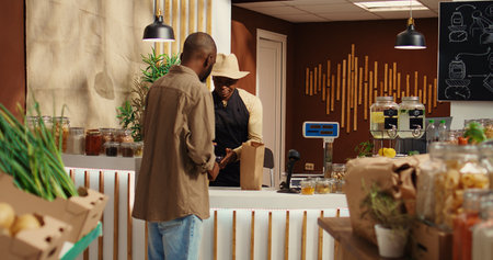 Male client paying for nonpolluting pantry supplies at market, supporting small business and...